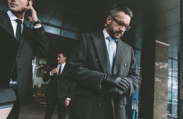 businessman looking at watch and standing with bodyguards